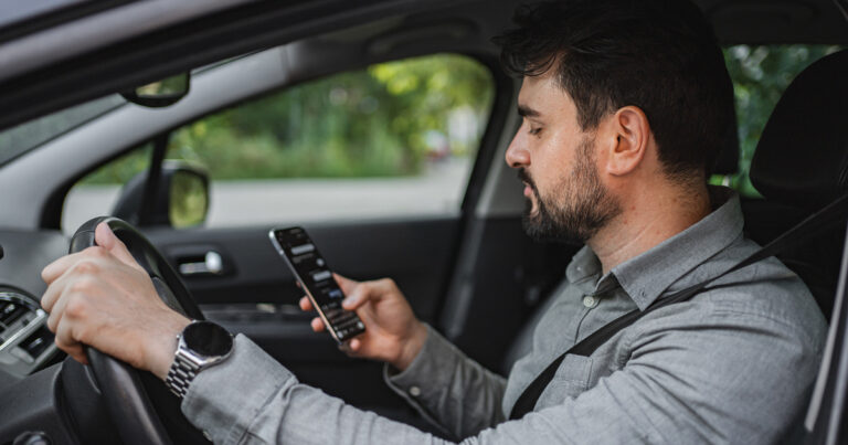 A man checking his phone screen while distracted driving.